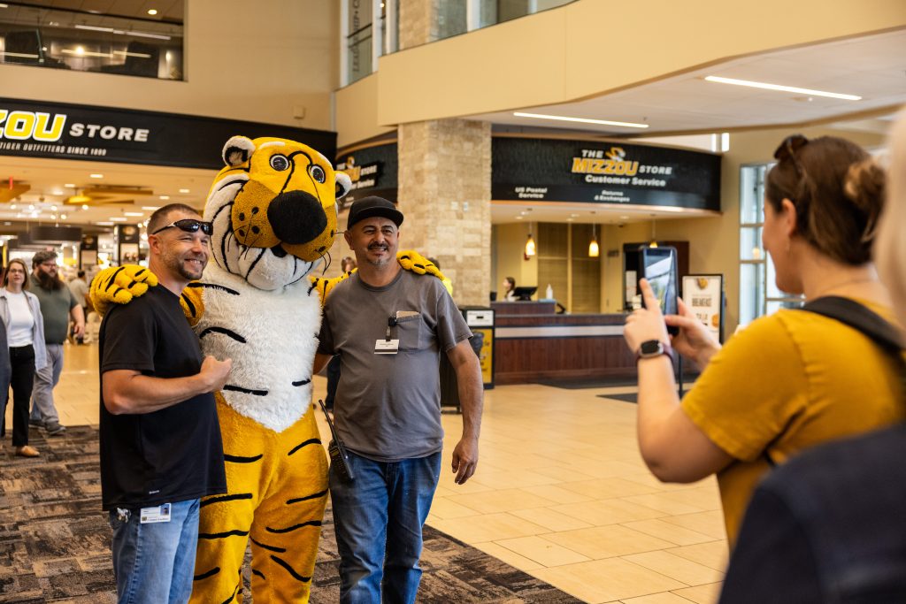 One person takes a photo of two staff members with Truman the Tiger