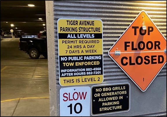 Close up view of signage posted outside a parking structure, including an orange diamond sign reading 